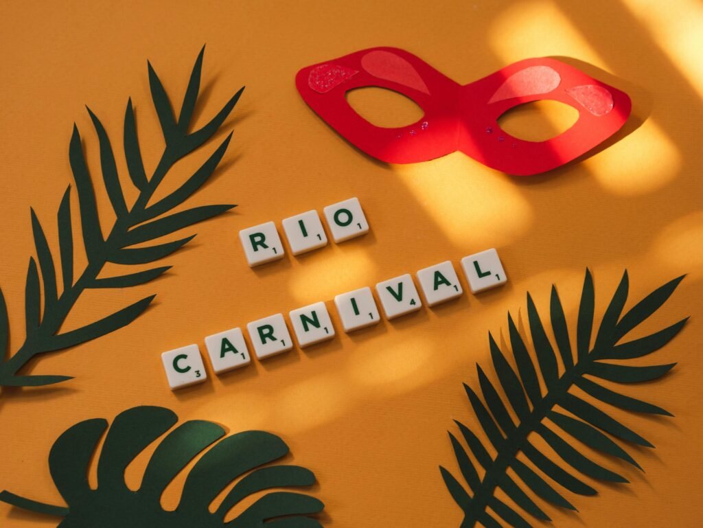 Artistic arrangement with letter tiles spelling 'Rio Carnival', tropical leaves, and a red mask on a yellow background.